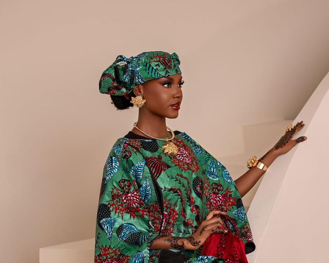Woman wearing a colorful traditional outfit with a headscarf, standing against a neutral background.